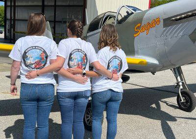 Chapter members showing the WAI Cleveland T-shirt in front of a vintage aircraft