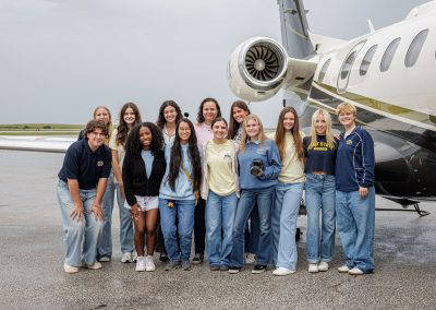 A group of teen girls poses in front of a business jet