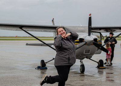 A woman strikes a playful pose in front of a small airplane