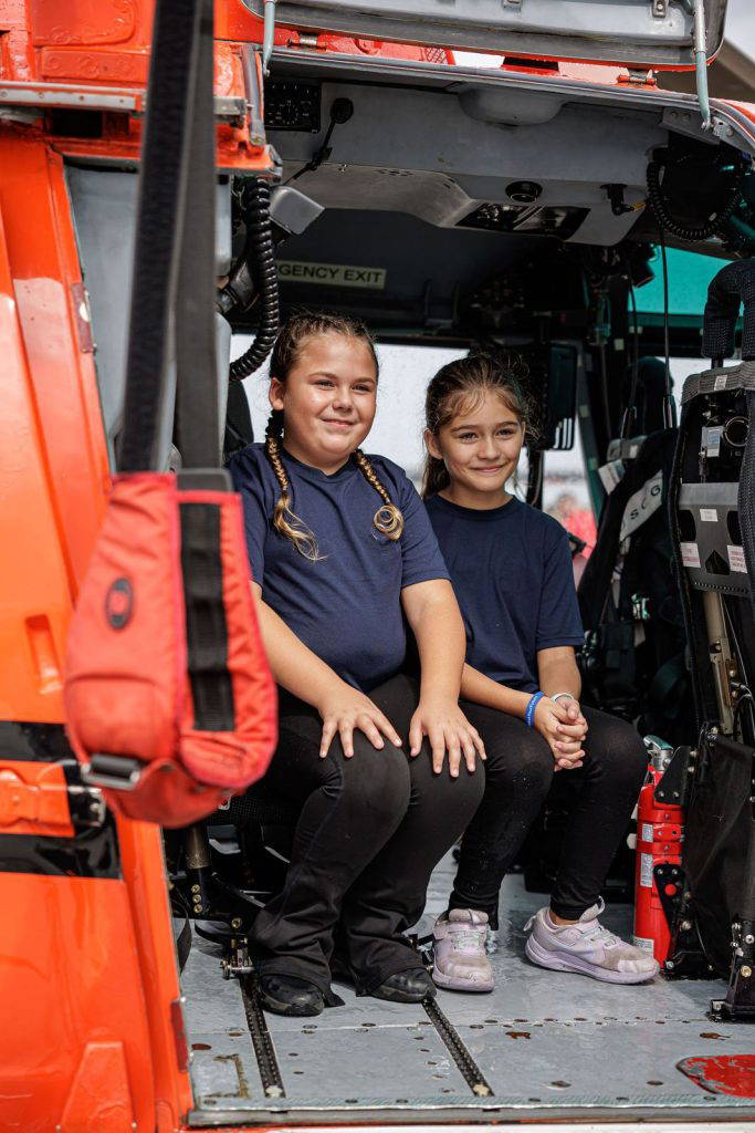 Two smiling girls sit inside the Coast Guard helicopter