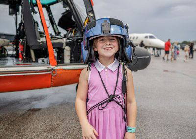 A girl wears a flight helmet beside the Coast Guard helicopter