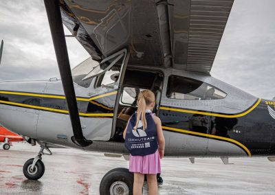 A girl stands under the wing of a small airplane
