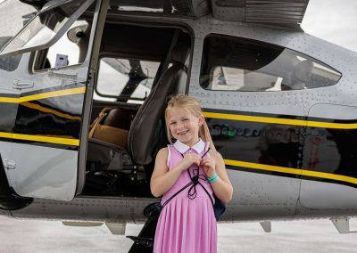 A girl smiles beside the wheel of a small airplane