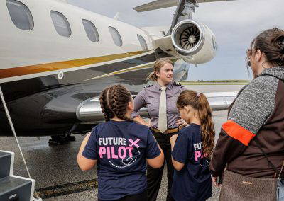 Girls in Future Pilot shirts talk with a pilot beside a jet