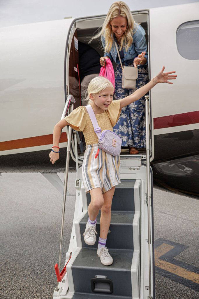 A girl waves as she comes down the stairs of a business jet