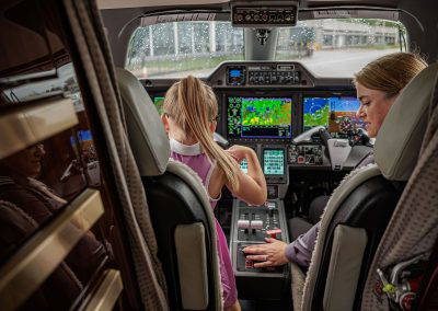 A girl sits in the cockpit with a pilot
