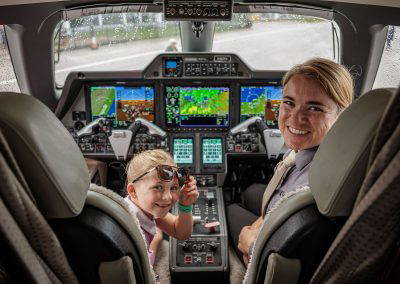 A girl smiles in the cockpit beside a pilot