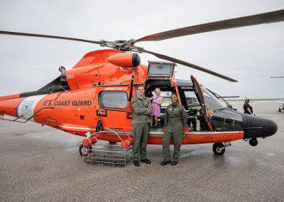 Coast Guard crew stand in front of their orange helicopter