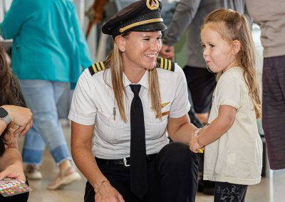 A pilot crouches to chat with a smiling young girl