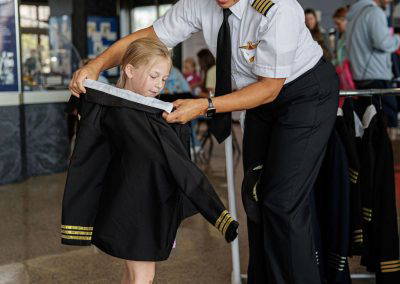 A pilot helps a young girl try on a pilot's jacket at Girls in Aviation Day