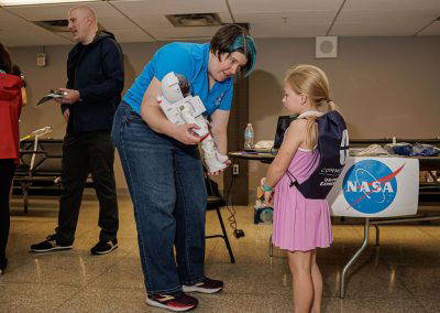 A volunteer greets a girl at the NASA table