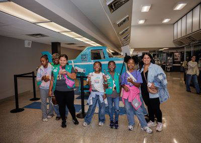 A group of girls poses in the terminal in front of an aircraft display